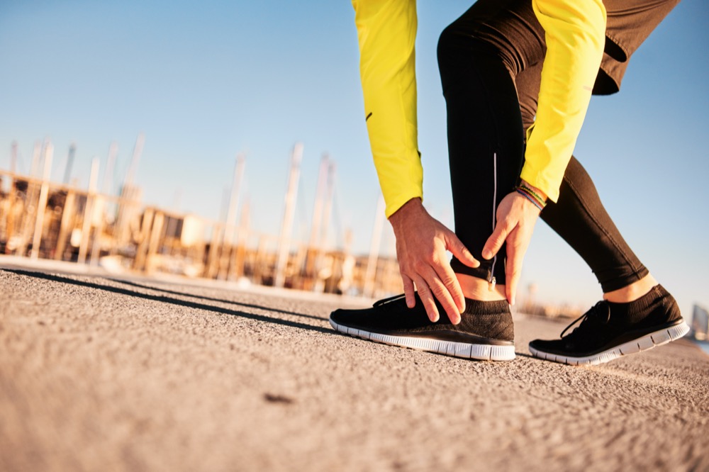 Runner holding injured ankle on outdoor pavement