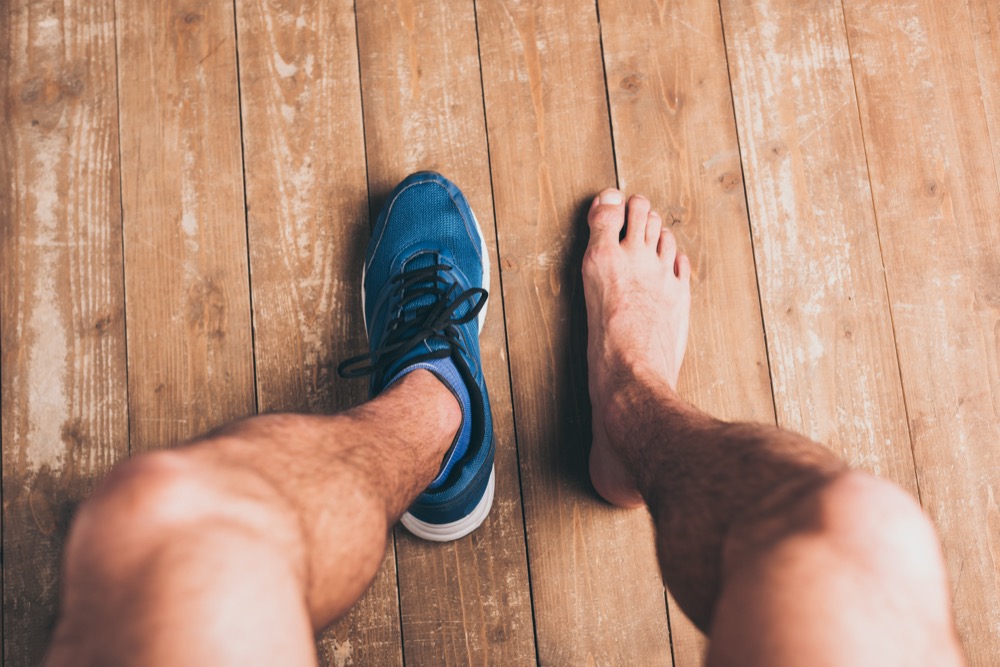 One foot in blue sneaker, one bare foot on wood floor