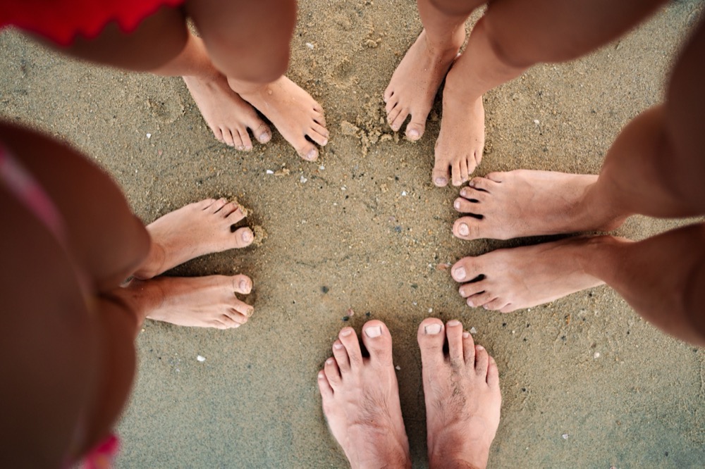 Group of bare feet standing in circle on sandy beach