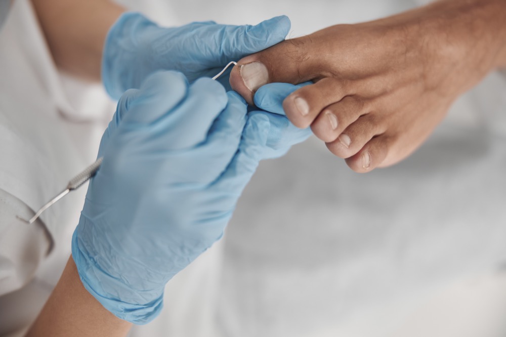 Podiatrist in blue gloves examining patient's toenails