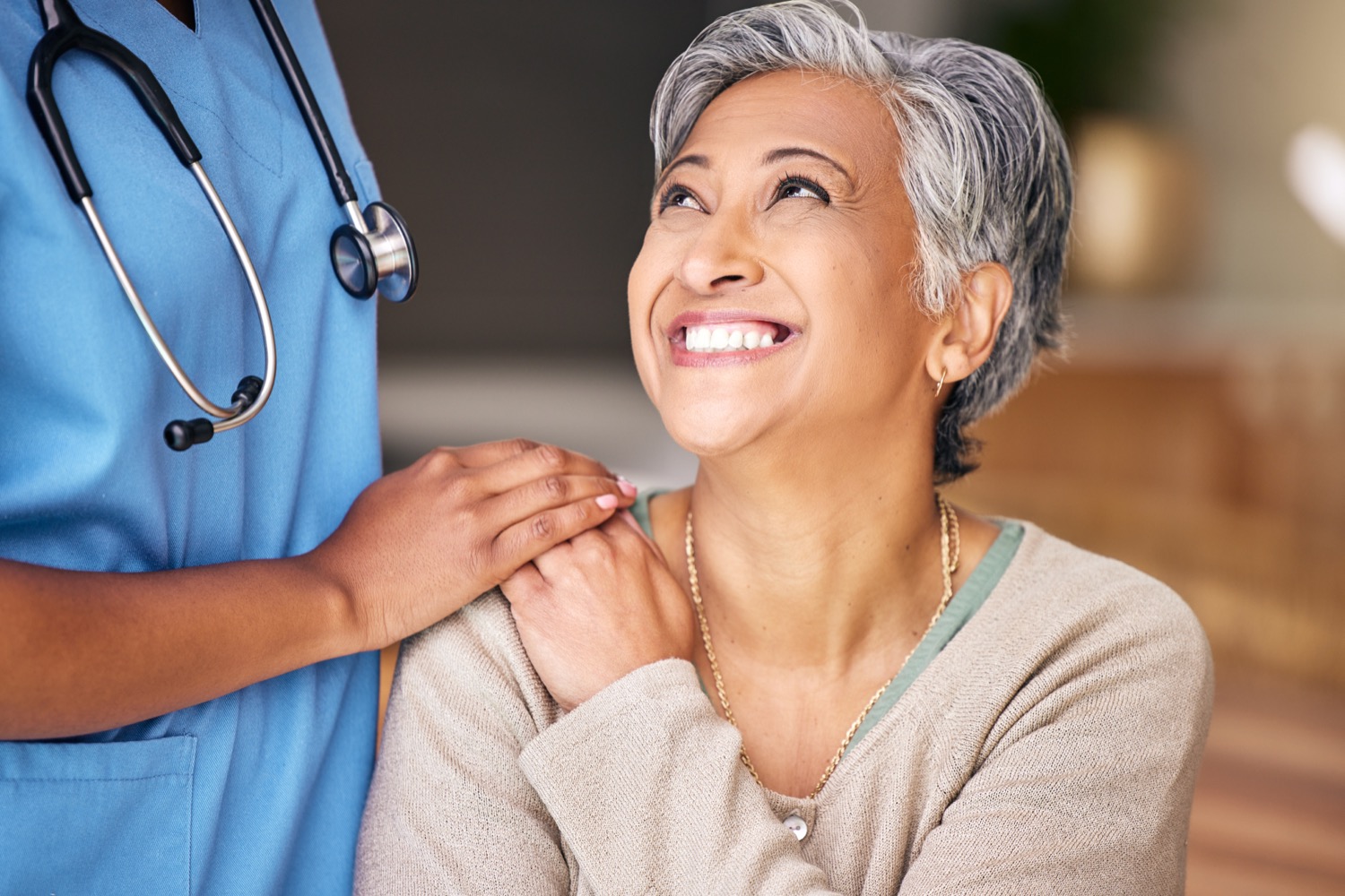 Smiling elderly patient with caring nurse in blue scrubs