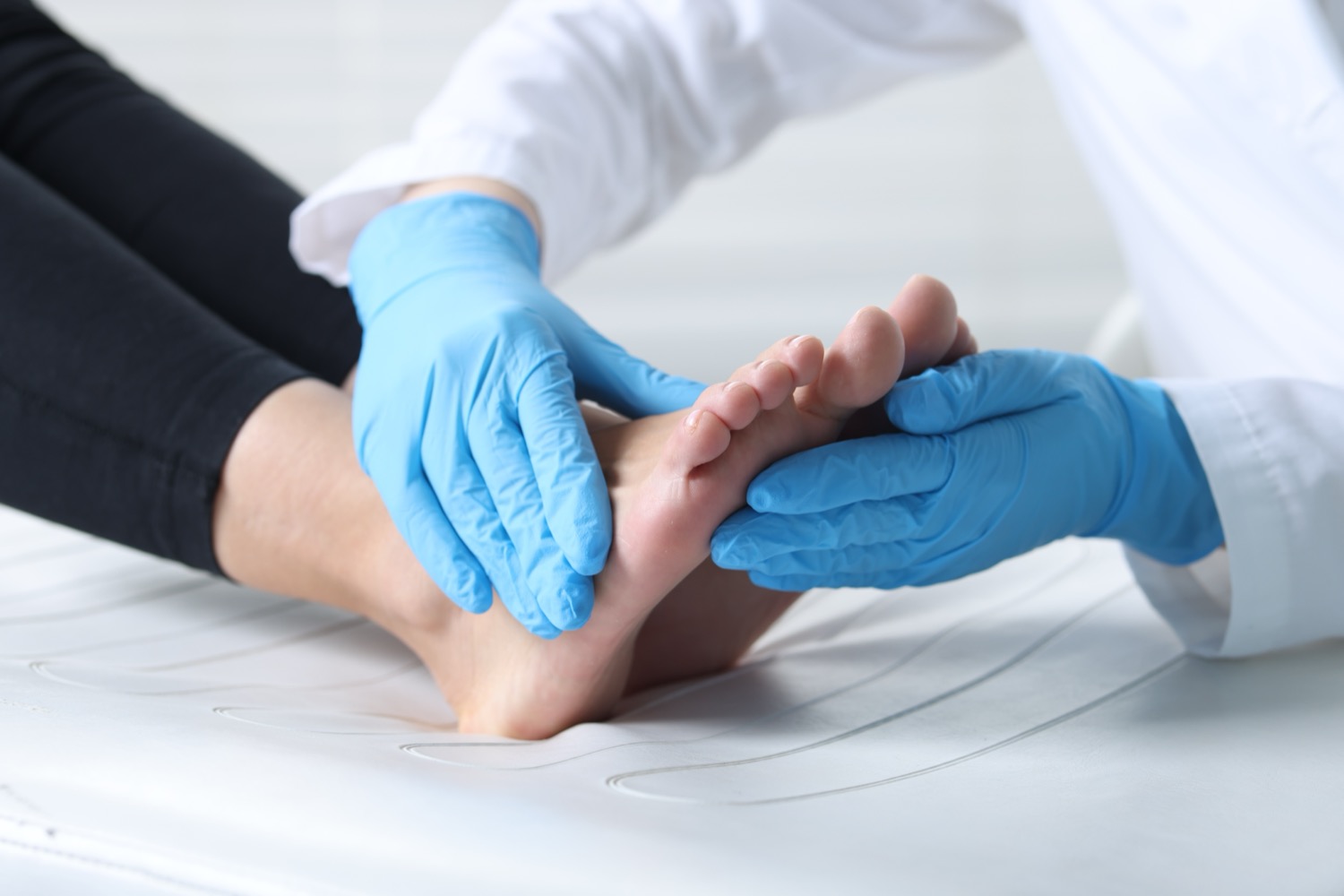 Doctor in blue gloves examining patient's foot closely