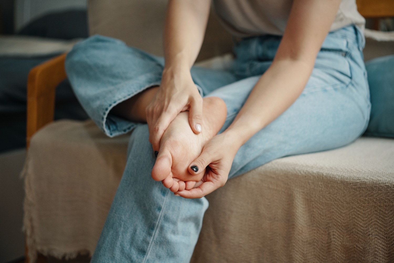 Woman in jeans massaging sore foot on couch