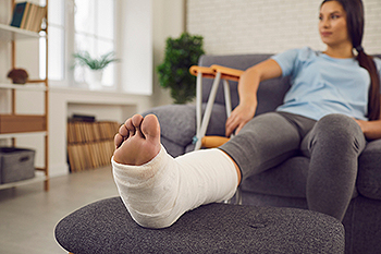 Woman resting with broken foot in white cast at home