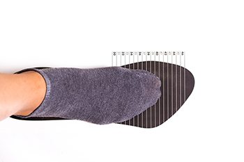 Foot in gray sock being measured on sizing tool
