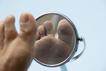 Person examining foot sole using a small handheld mirror