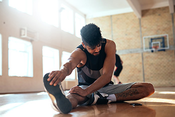 Athlete stretching on basketball court floor before practice