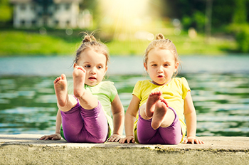 Two young twin girls sitting by a sunny lakeside