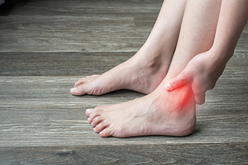 Person holding painful red glowing ankle indicating injury