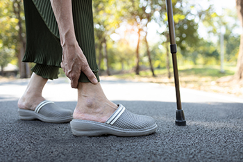 Elderly person holding ankle with walking cane nearby