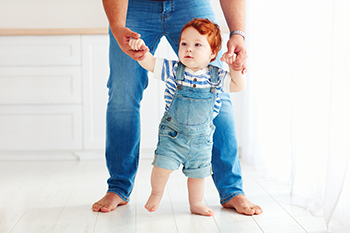 Redhead toddler taking first steps with parent's help