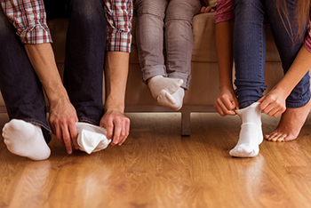 Three people putting on white socks on wooden floor