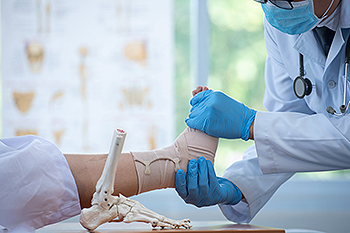 Doctor bandaging patient's ankle in medical office